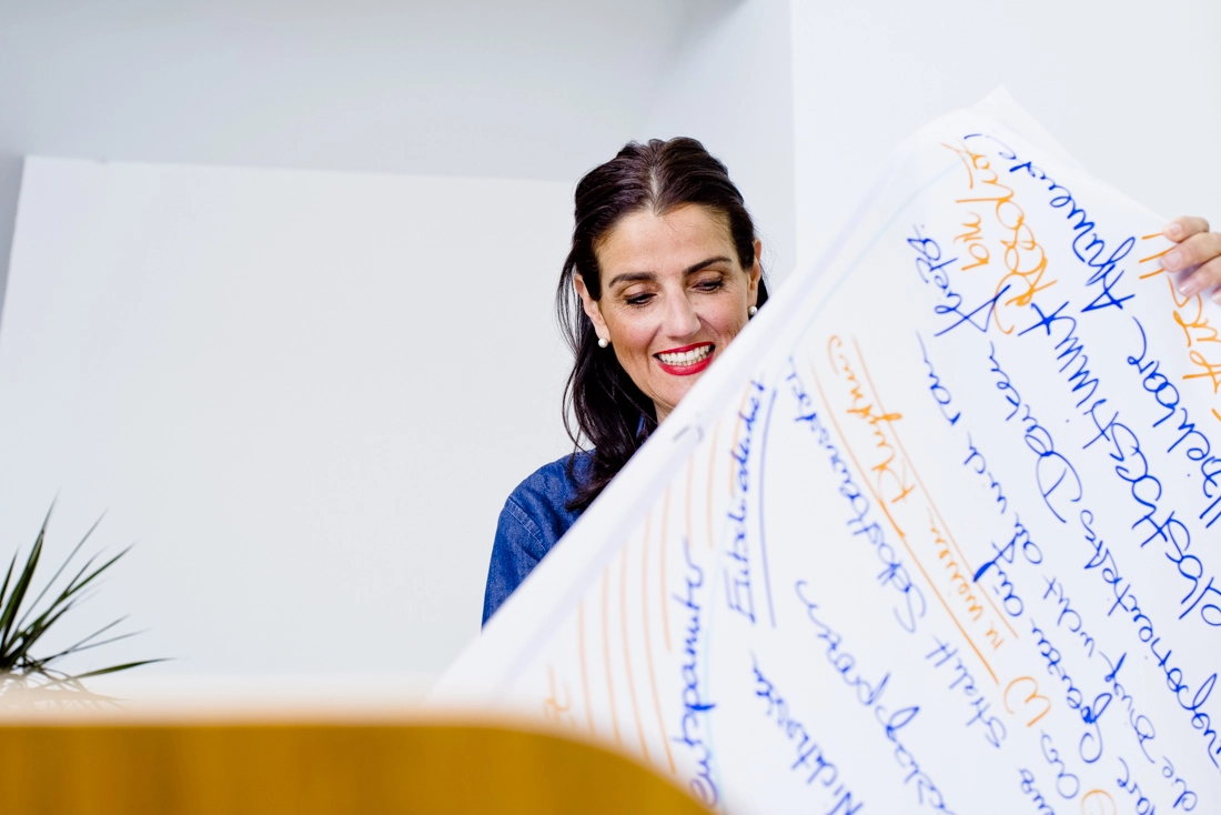 Irena Mila Steinmeier hält lächelnd ein beschriebenes Flipchart-Blatt