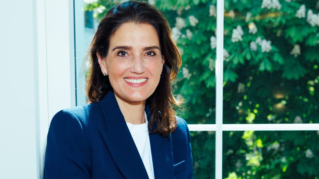 Irena Mila Steinmeier lächelnd im Blazer vor grünen Blättern – Online Business Coaching