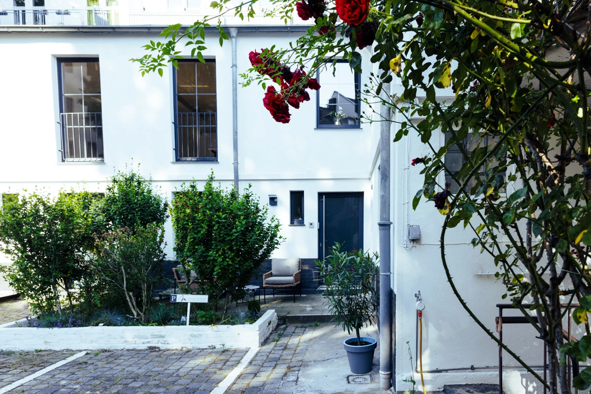 Eingang zum Raum für Menschen in Düsseldorf: weißer Hinterhof mit Rosen und Sitzecke